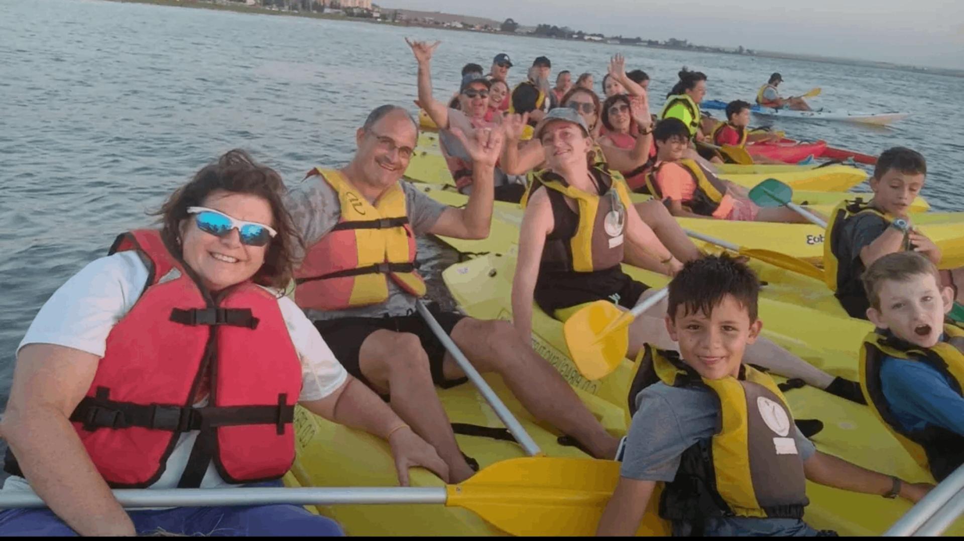 Personas con chalecos salvavidas saludan a la cámara en piraguas