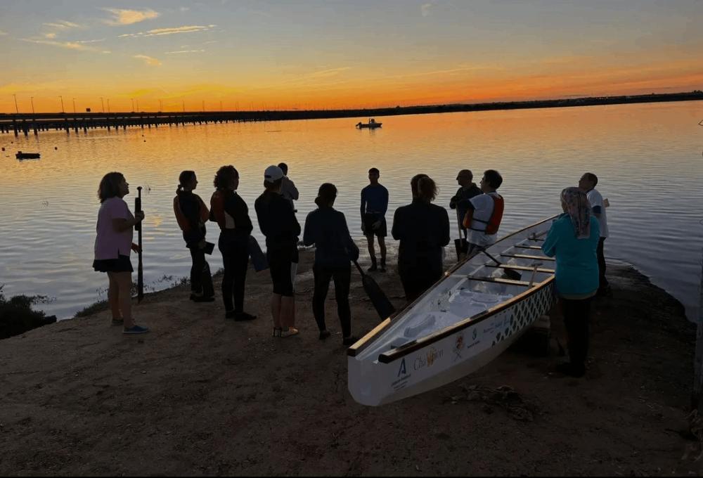 Personas con trajes de neopreno en una playa al atardecer